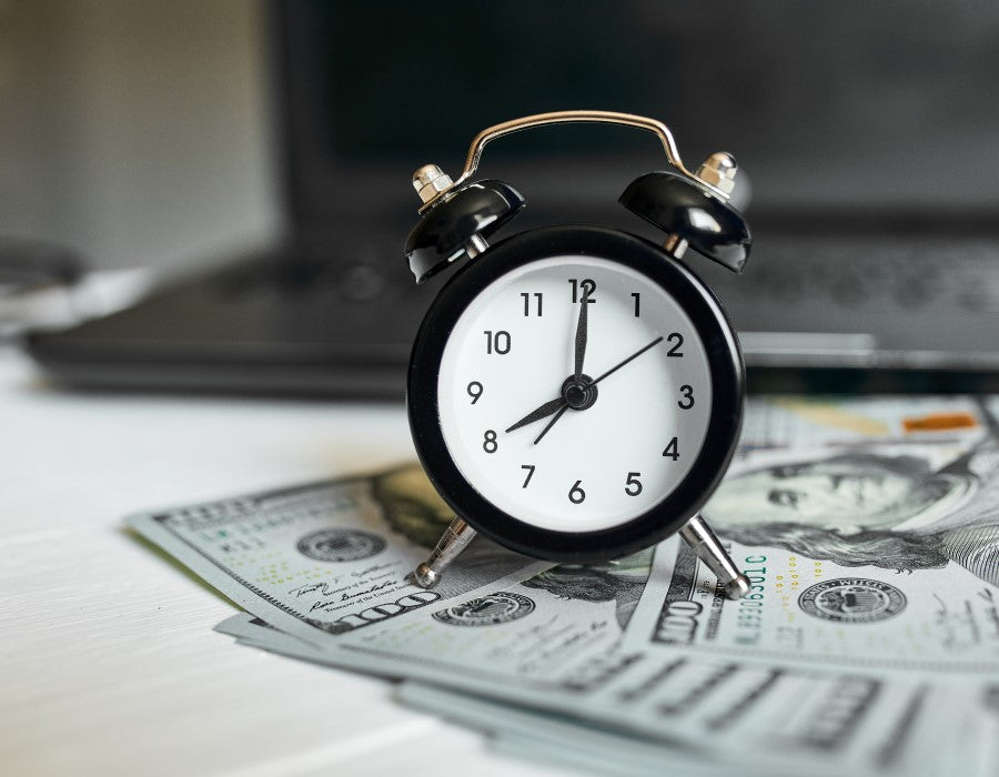 An alarm clock sitting on a pile of money highlighting how PermaSafe Clean and save you both time and money while cleaning your environments.