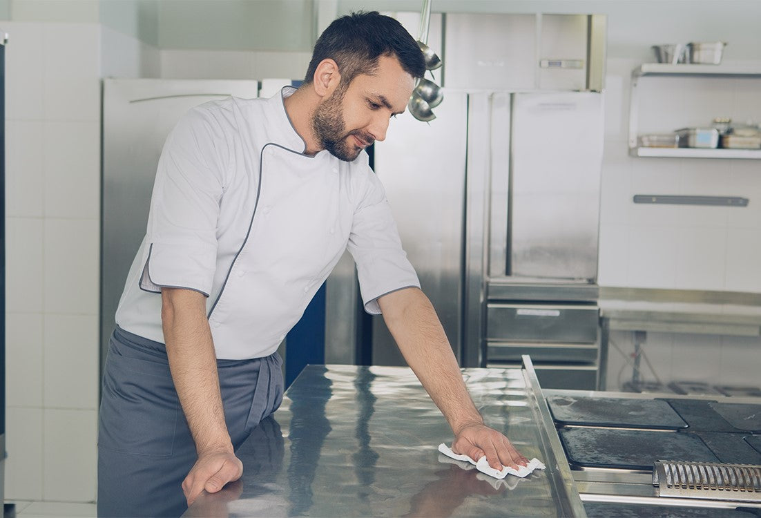 A person in a commercial kitchen cleaning a surface using PermaSafe products, which are EPA registered as safe for food contact surfaces.