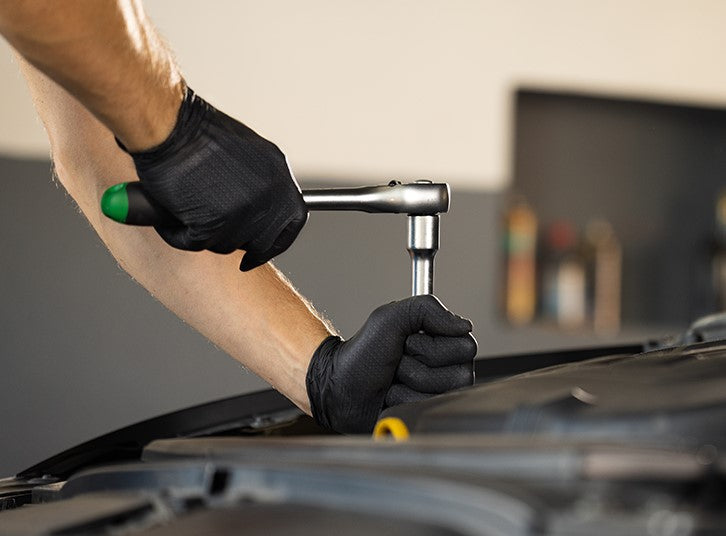 PermaSafe industrial-strength nitrile gloves provide superior grip using our proprietary raised diamond texture as shown by a auto mechanic wearing them while working on a car.