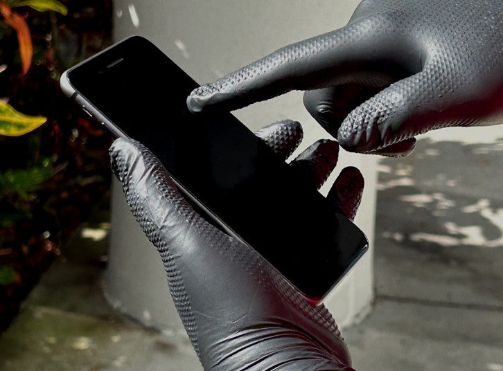 a person wearing a pair of PermaSafe industrial-strength nitrile gloves whose fit and feel is precise enough to allow the use of touch screen devices as this person is doing